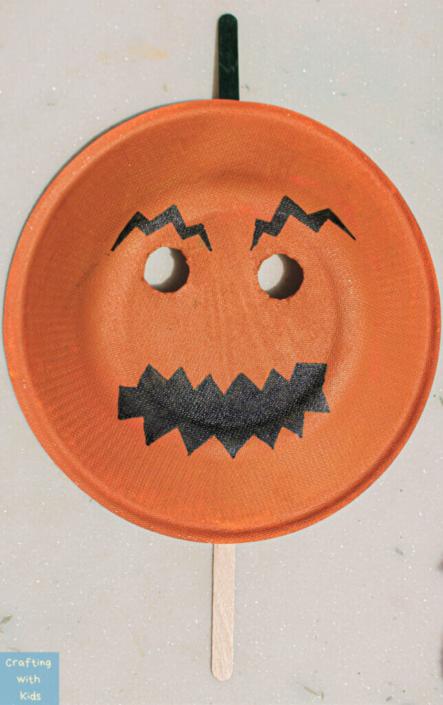 Amazing Halloween Pumpkin Mask Made With Paper Plate, Black Paint & Popsicle Sticks - Preschoolers can have fun crafting with Halloween paper plates.