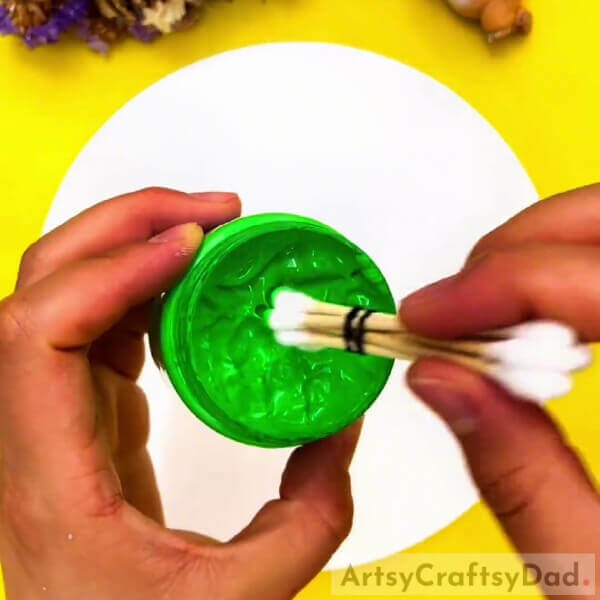 Dipping The Buds Into Green Paint- Earbud stamping can create colorful tree art for children.
