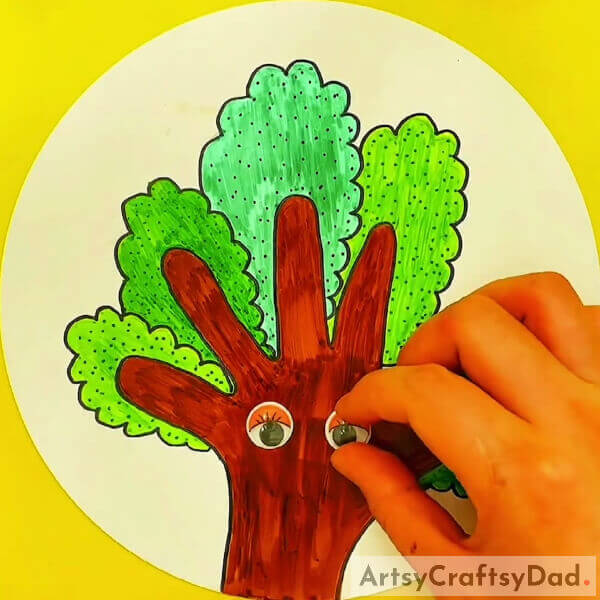 Now, get the googly eyes and paste them on the bark - Kids' Guide to Crafting Trees with Hand Outlines 