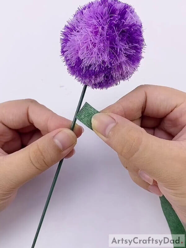 Wrap a dark green strip around the stick - Crafting A Ribbon Pom-Pom Flower With Kids: A Tutorial